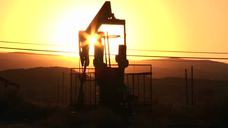 an oil derrick pumps at sunset