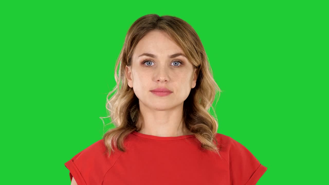молодая женщина в красной футболке идет, смотрит на камеру на зеленом экране, хроматический ключ