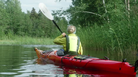 blonde girl with a yellow life jacket leisurely paddling between islands and reeds, finland, vaasa, kvarken archipelago