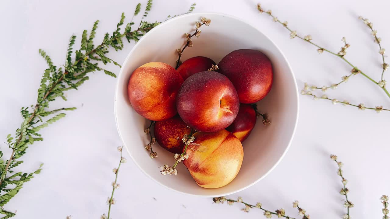Pêches dans un bol blanc avec un arrangement floral