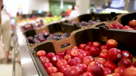 red apples in a supermarket aisle with bustling shoppers and bright lighting, showcasing fresh produce in a lively environment