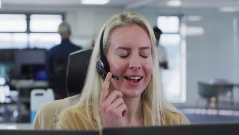 Woman-wearing-headset-talking-while-sitting-on-her-desk-at-office