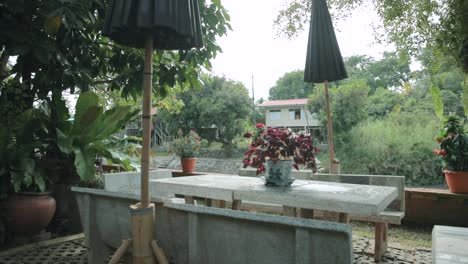 Slow-Motion-Panning-Shot-of-a-Marble-Table-with-Flowers-at-a-Garden-Next-to-a-Canal-in-Ayutthaya,-Thailand