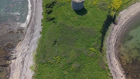 aerial revealing shot of coastal martello tower surrounded by green grass on shenick island in ireland