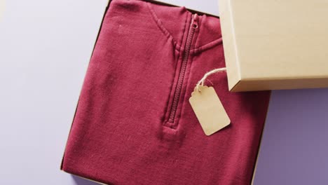 video of close up of red sweater with tag in box on purple background