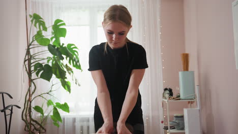 blonde woman wearing black shirt massaging client on table in softly lit wellness room decorated green indoor plant, anatomical chart, and spa equipment for a tranquil healing ambiance