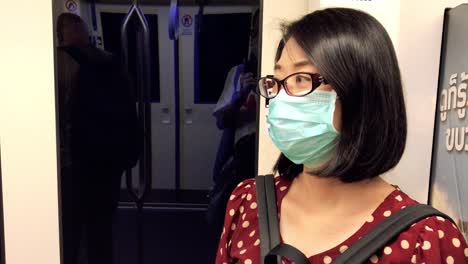 thai middle-aged woman wearing a medical mask while standing in the subway train or mrt of bangkok, thailand