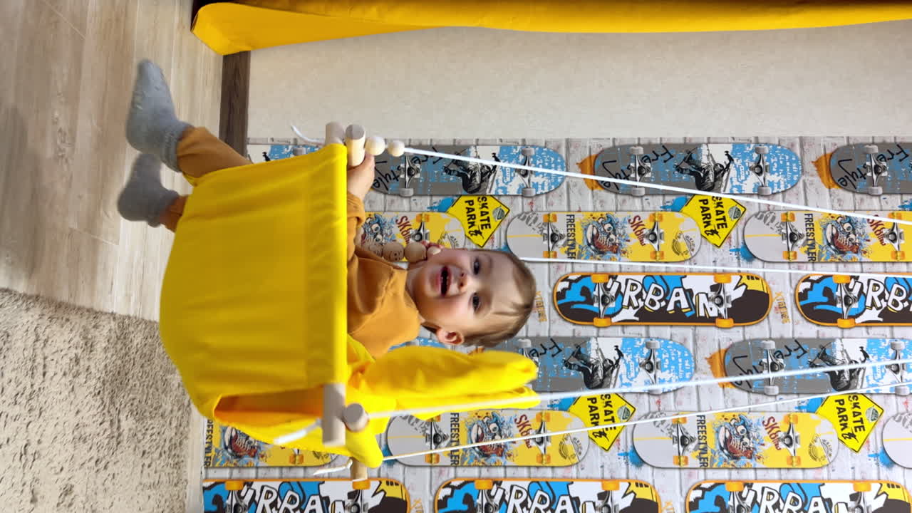 Fun time on the yellow swing. Little happy baby is swinging at home. Close up. Vertical screen.
