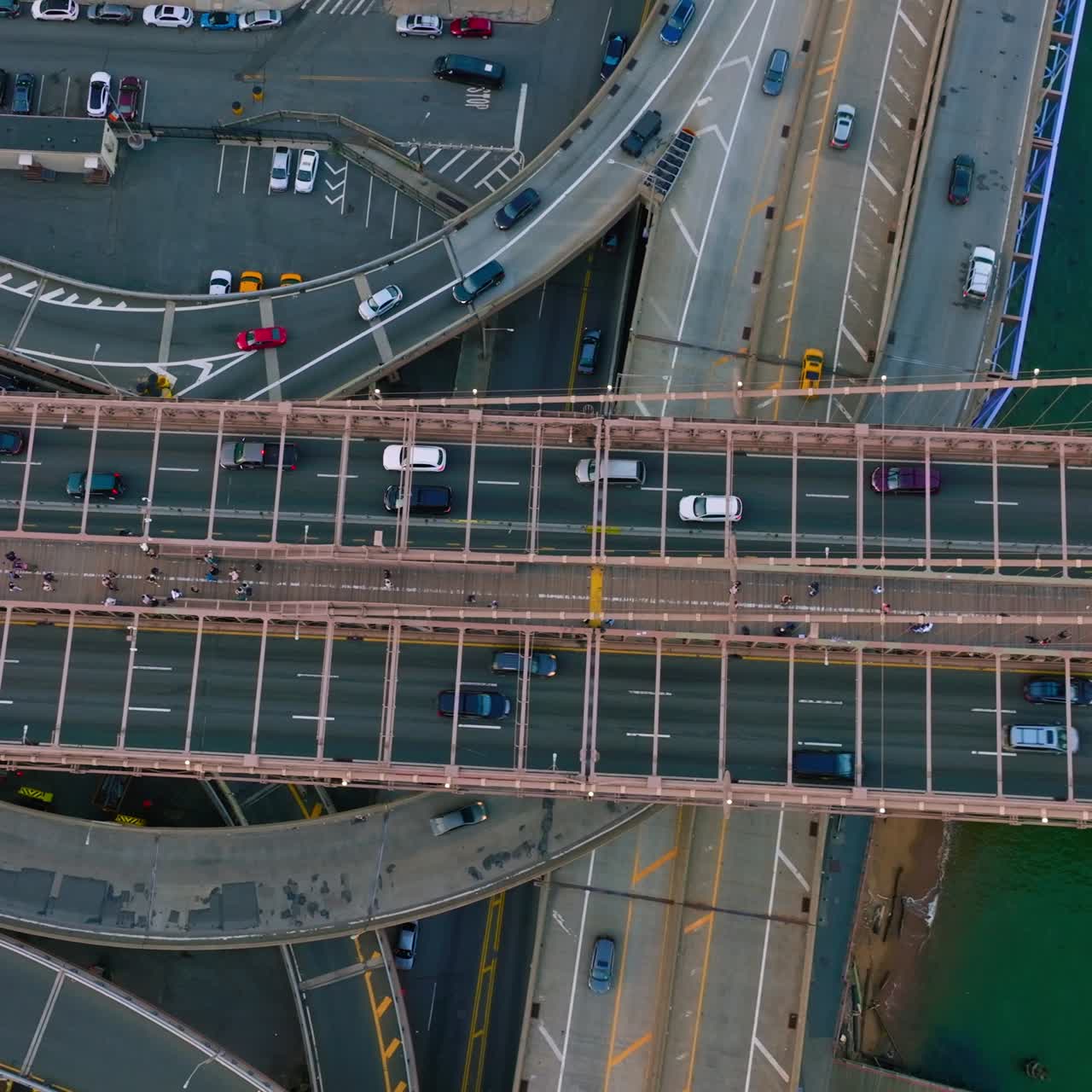 Multiple cars moving quickly over the huge bridge and roads under it. Heavy traffic and car parking lots in a big city. Top view