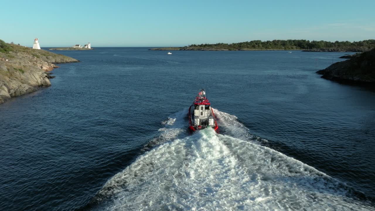 A tugboat moves steadily through calm waters, surrounded by rocky shores and small islands. Distant lighthouses stand tall against a clear blue sky, marking safe passage