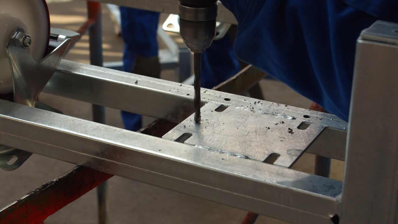 человек сверлит отверстие в металлической раме с помощью электрической отвертки в мастерской, статичный вид