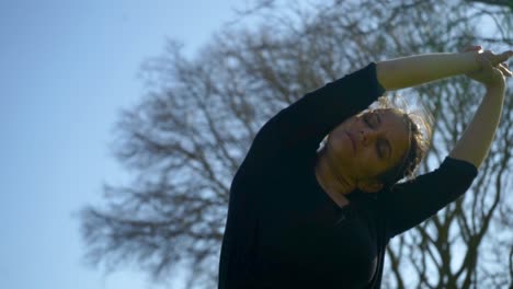 chica atractiva y deportiva con los ojos cerrados estirándose en el parque