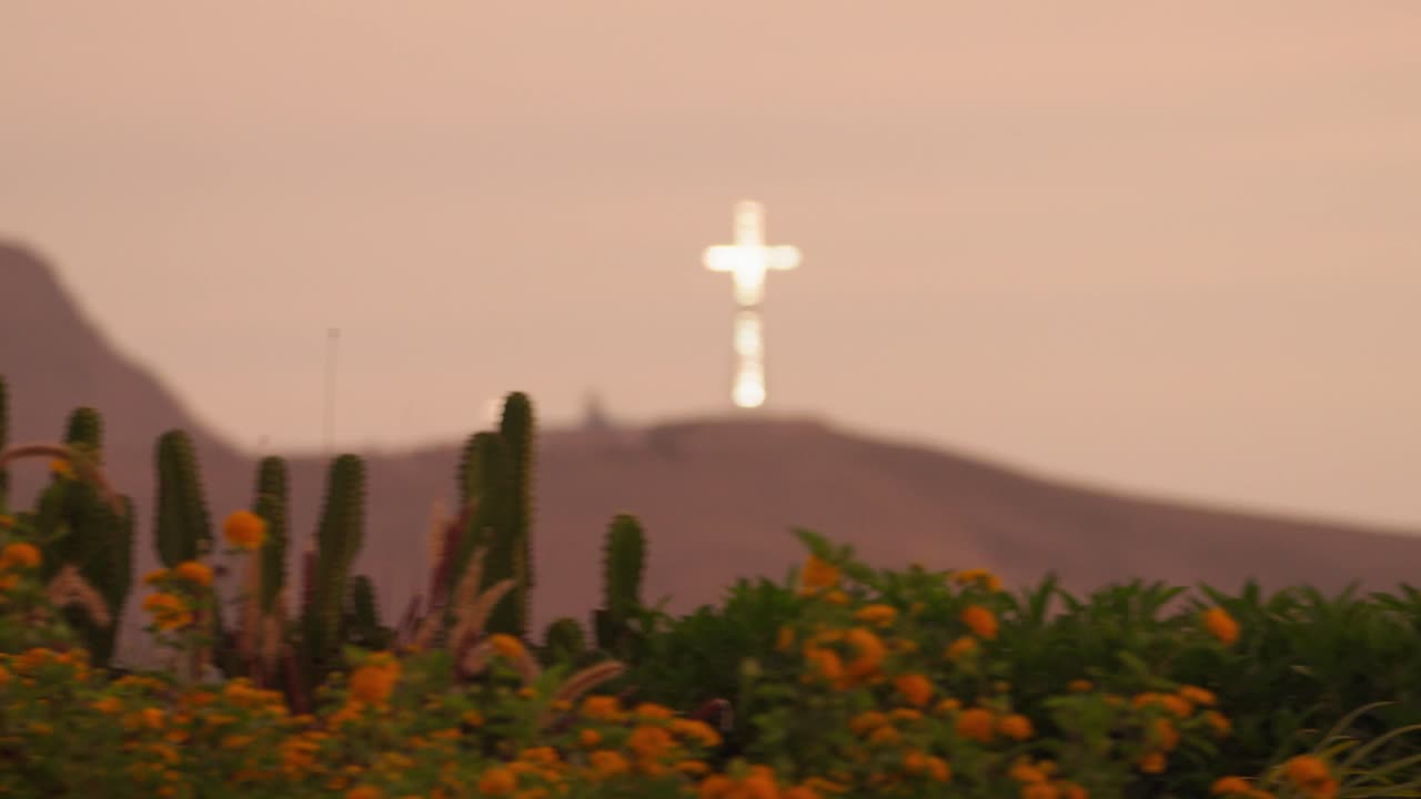 Scenic pan of Barranco Park, Lima, at sunset. The iconic illuminated Chorrillos Cross stands in the background under golden hour light, showcasing Peru's urban evening charm