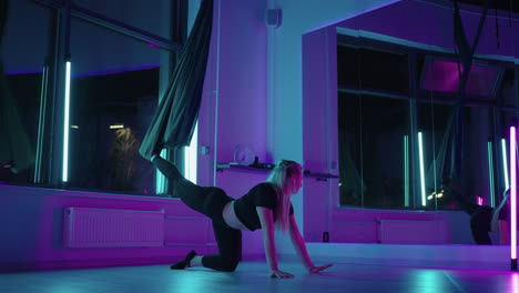 a woman does yoga and stretching on a hanging hammock in neon light. young pretty slim body fitness girl practicing fly yoga in the gym.