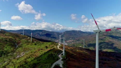 static view of white wind turbines moving over a hilly terrain with thick green vegetation with white clouds passing by at daytime