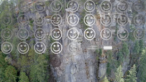 digital composition of rows of multiple smiling face emojis against aerial view of a mountain