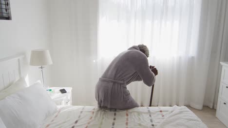 senior man holding his walking stick while sitting on bed at home