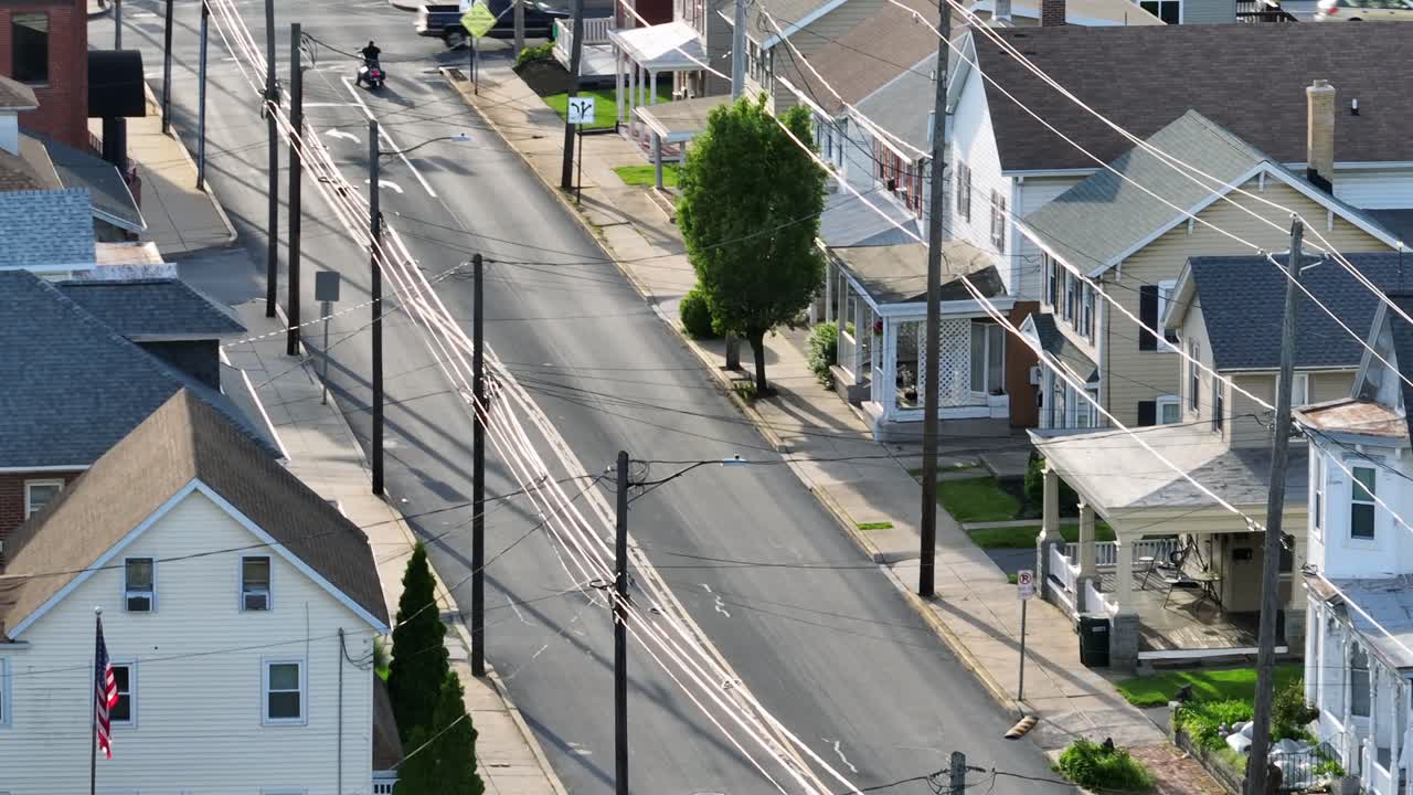 American family houses with porch at entrance during sunny day in Akron, Pennsylvania. Aerial tilt up shot. Row of houses and traffic on junction. Waiting motorbike on road. Wide shot.