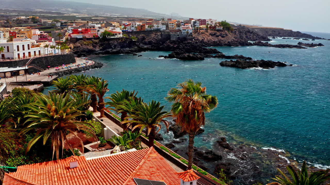 Aerial drone shot over the beautiful volcanic rocky coastline of Tenerife, Canary Islands, Spain. High view of the turquoise sea volcanic coast and the local towns. Summer holidays destination.