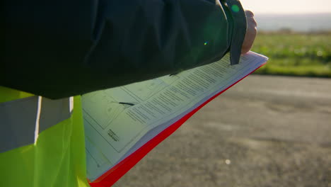 ingeniero con chaleco reflectante de seguridad leyendo el manual en el portapapeles mientras sostiene un bolígrafo, primer plano de mano