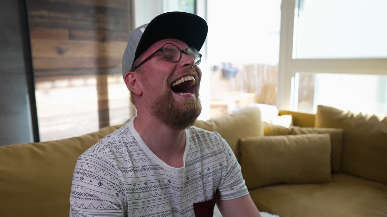 금발, 밀레니엄 세대의 남자가 텔레비전을 보고, 큰 소리로 웃으며, 슬로우 모션 확대