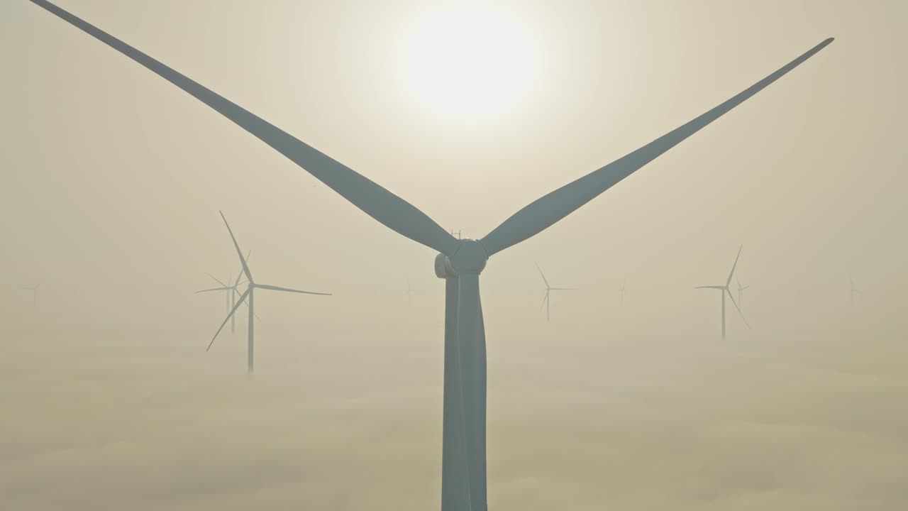 Parco eolico che genera energia pulita sopra le nuvole durante un'alba nebbiosa