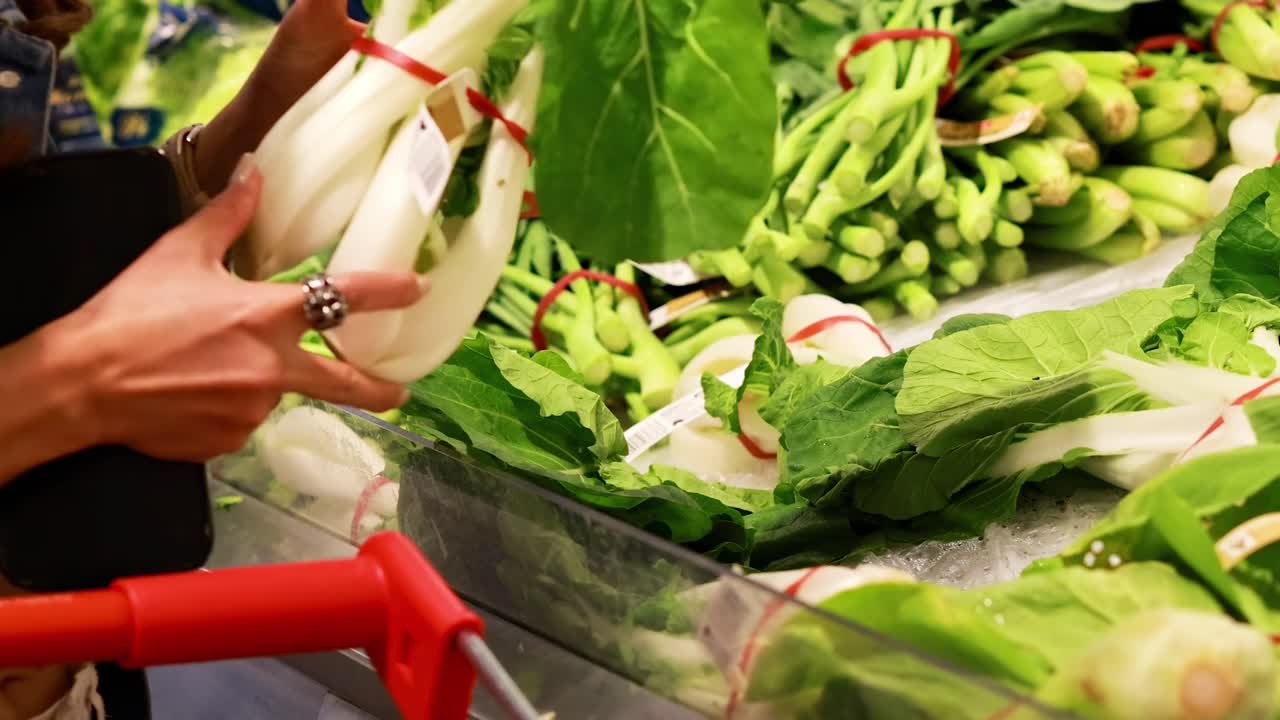 A person examines and picks fresh bok choy from a vibrant grocery store display.