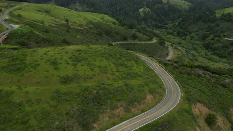 aerial pull back shot of a very windy section of highway 1 in northern california with cars driving past