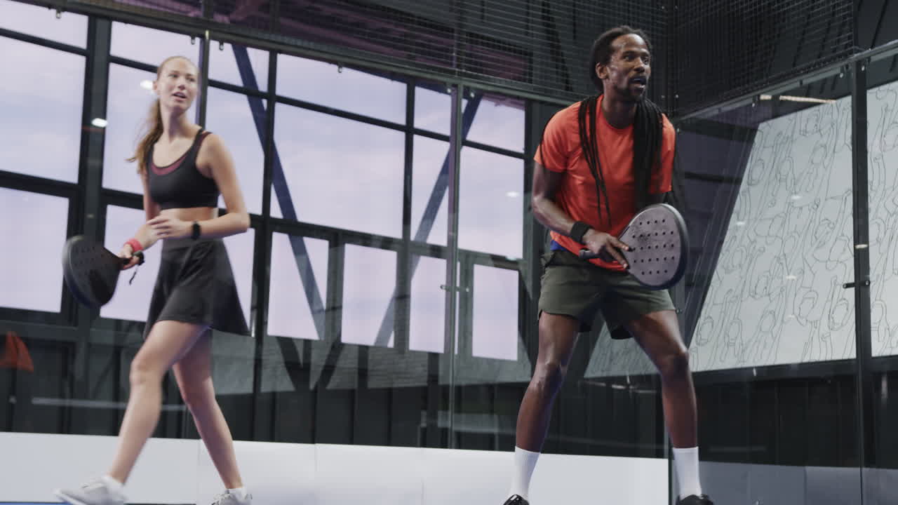 Olika spelare njuter av en intensiv padelmatch på inomhusbana, med fokus på spelet.