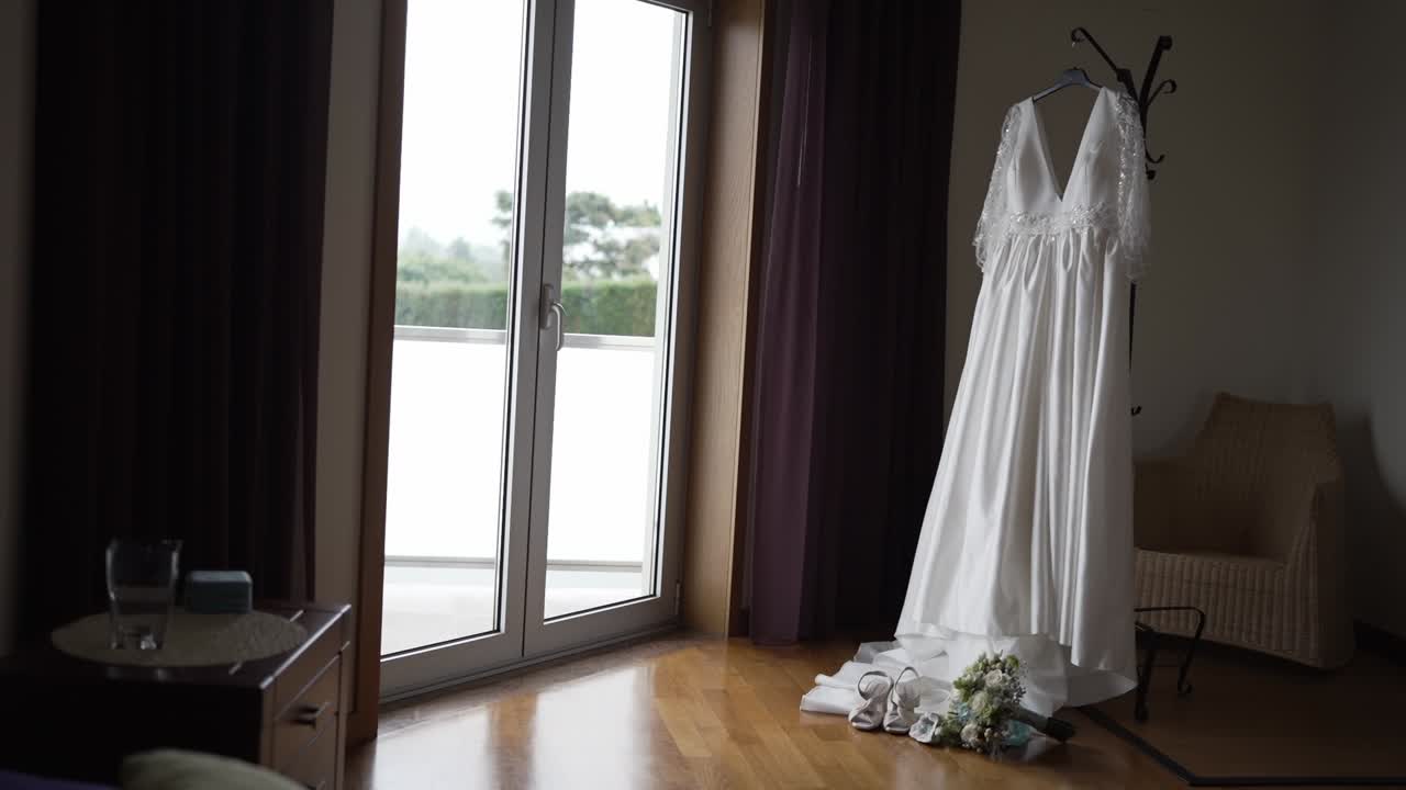 white wedding dress with shoes and bouquet arranged near a window in soft light