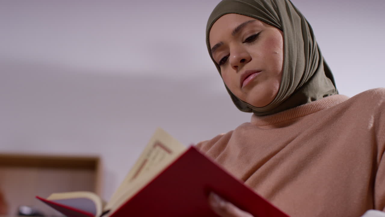 mujer musulmana con hijab sentada en el sofá en casa leyendo o estudiando el corán 1