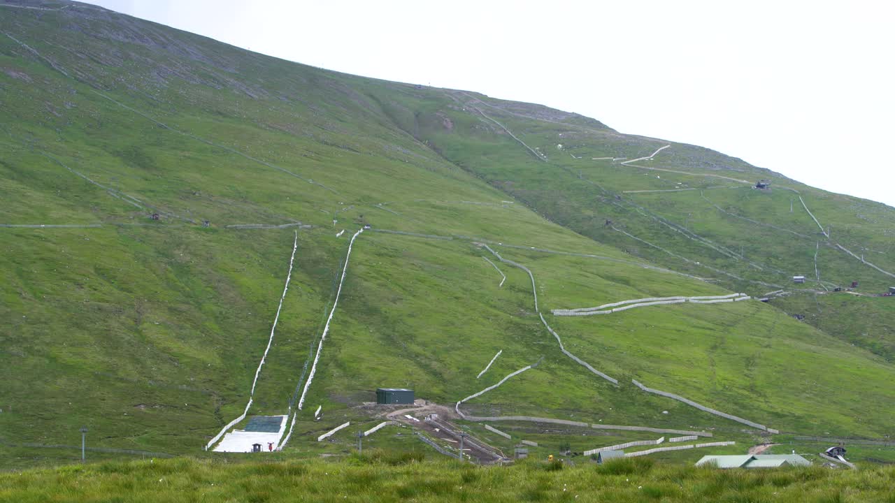 스키는 눈이 내리지 않는 여름날 스코틀랜드 벤 네비스의 겨울 스포츠 지역에 있는 푸른 잔디밭에서 뛰고 있습니다.