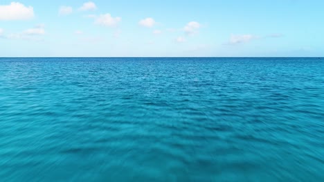 Quick-low-flying-aerial-dolly-above-caribbean-blue-water,-light-blue-to-dark-blue-gradient-on-horizon