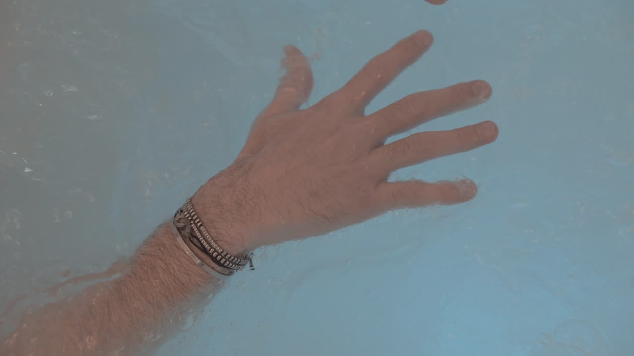 primer plano de las manos de un hombre que se relaja en un jacuzzi, sus dedos están extendidos y pulseras en sus muñecas