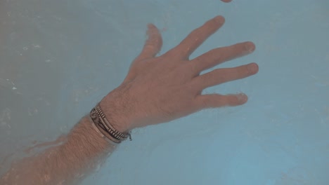 close-up of the hands of a man who is relaxing in a jacuzzi, his fingers are spread and bracelets on his wrists