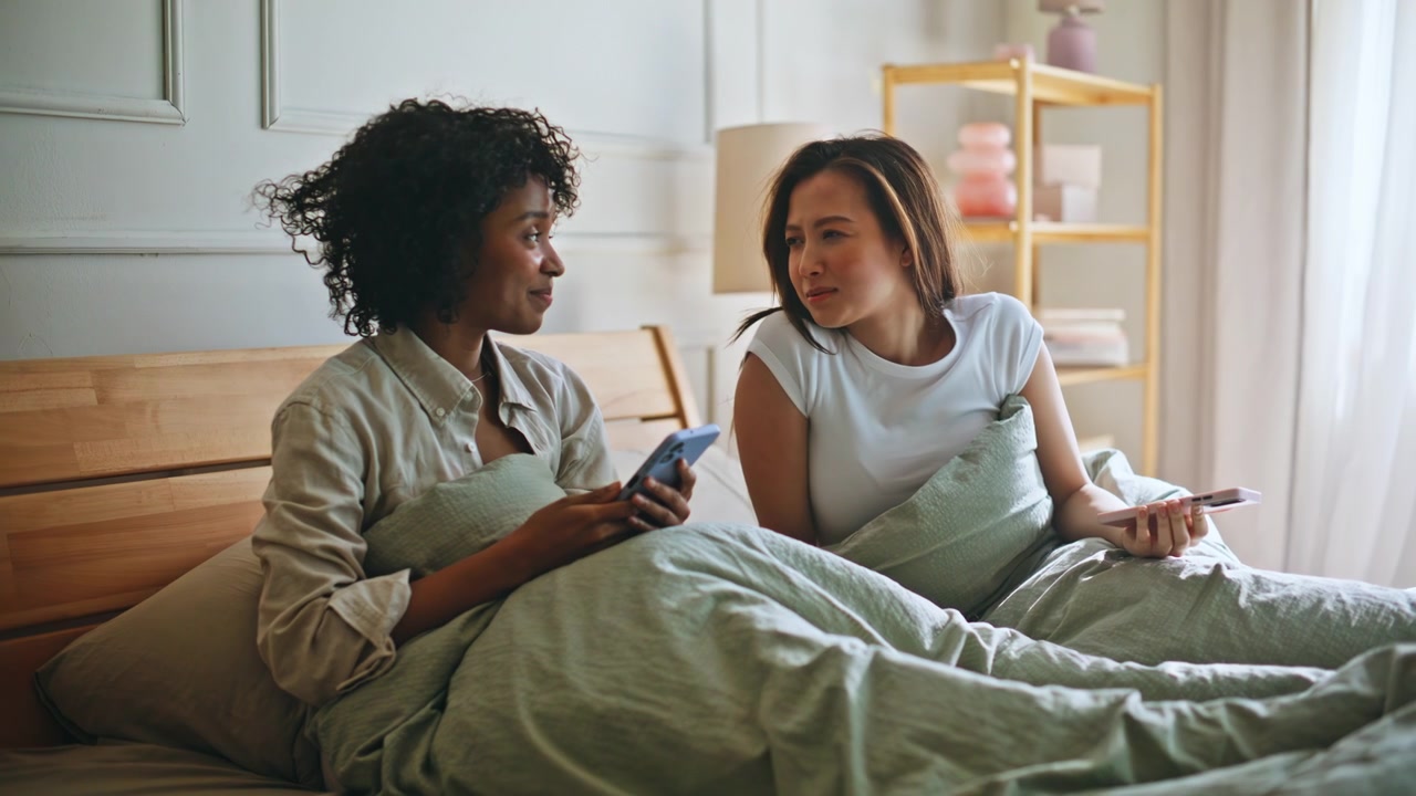 Upset woman leaving bed after phone quarrel. Female couple conflict bedroom.