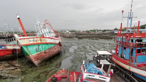 thai fishing trawlers grounded on low tide in the harbor near chonburi, thailand