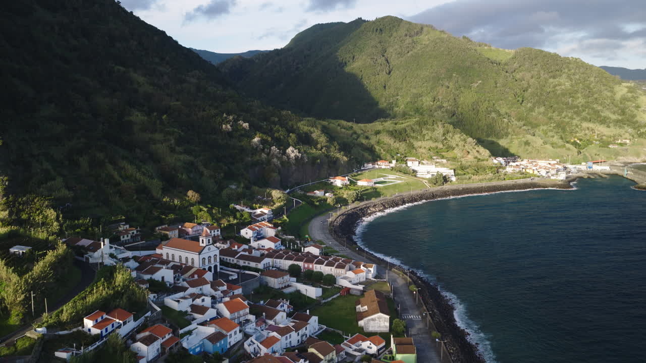 Vista aerea di un pittoresco villaggio costiero con tetti rossi e colline verdeggianti