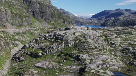 fotografía aérea, subiendo desde un pequeño lago poco profundo en noruega, sobre un paisaje montañoso rocoso y cubierto de musgo, revelando una vasta cordillera y un gran lago, con una presa hidroeléctrica