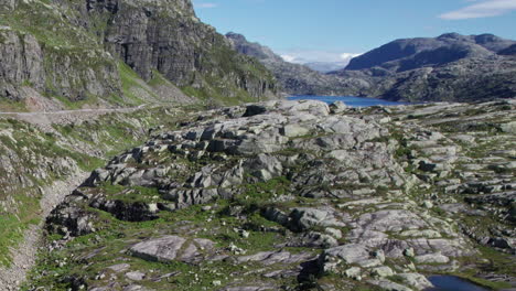 aerial shot, climbing from a small, shallow lake in norway, over a rocky, moss covered mountain landscape, revealing a vast mountain range and a large lake, with a hydroelectric dam