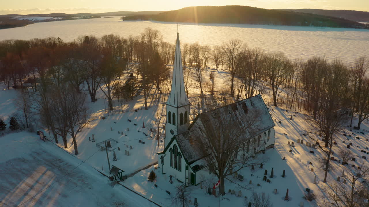 Scenic winter aerial circling over a snow covered church at sunset.