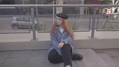 two friends have fun taking pictures in the street. the redhead woman model poses sitting on the sidewalk for her photographer friend and smile
