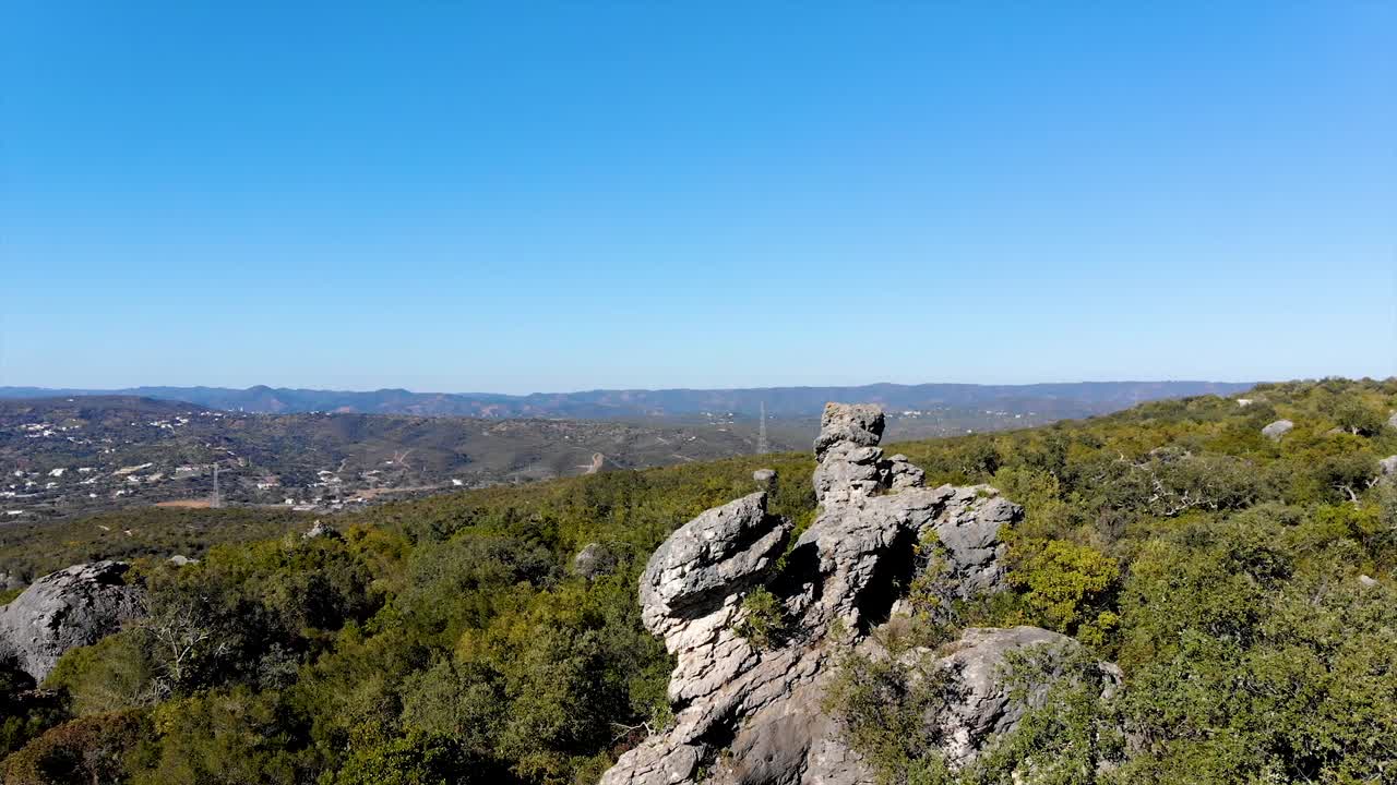 formación rocosa sobre un paisaje verde, fondo con colinas y algunas casas lejos
