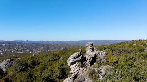 formación rocosa sobre un paisaje verde, fondo con colinas y algunas casas lejos