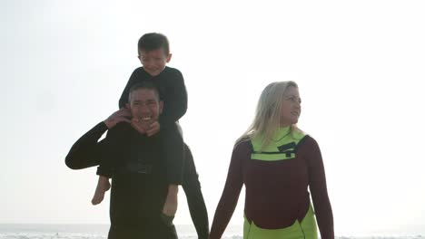 happy family in wetsuits walking on beach