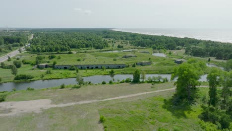 aerial establishing view of abandoned historical concrete seaside fortification buildings, southern forts near the beach of baltic sea in liepaja, sunny summer day, drone shot moving forward tilt down