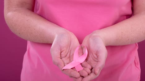 Video-De-La-Sección-Media-De-Una-Mujer-Caucásica-Sosteniendo-Una-Cinta-Rosa-De-Concientización-Sobre-El-Cáncer,-Con-Fondo-Rosa