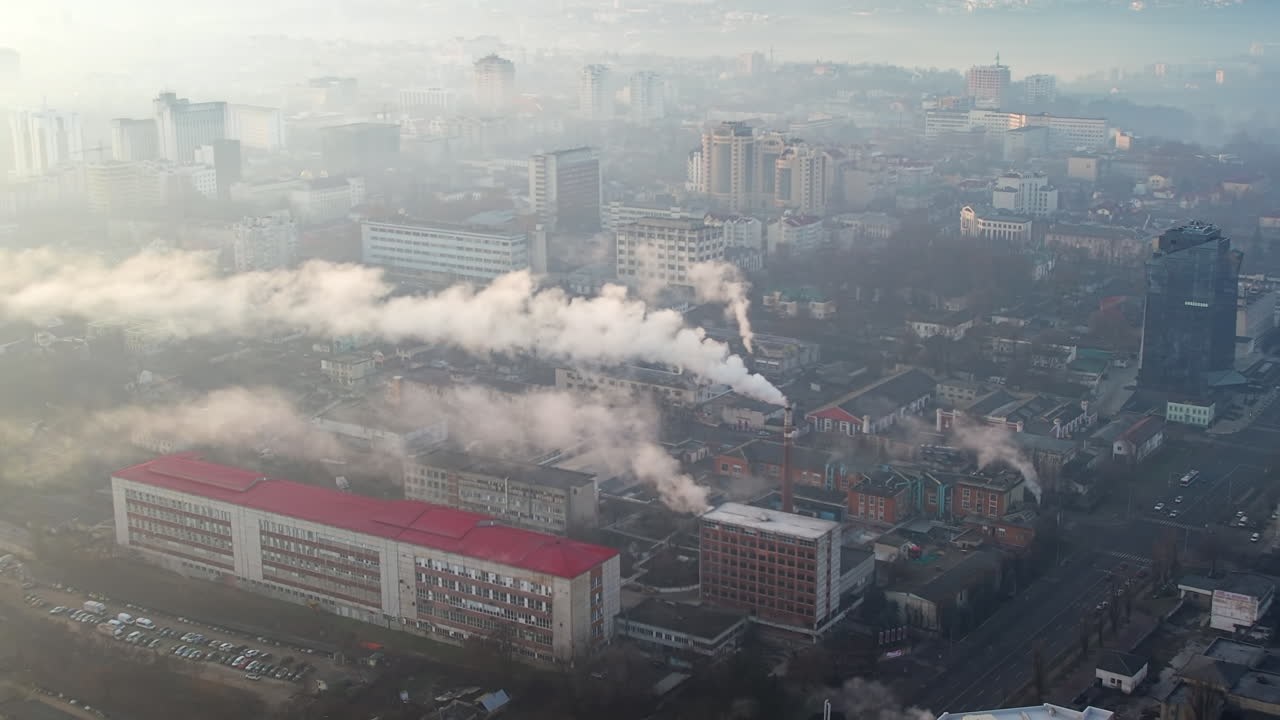 Tampilan drone udara dari fasilitas produksi di Chisinau saat matahari terbit, Moldova. Pemandangan kota dengan beberapa bangunan, pipa dengan uap yang berjatuhan