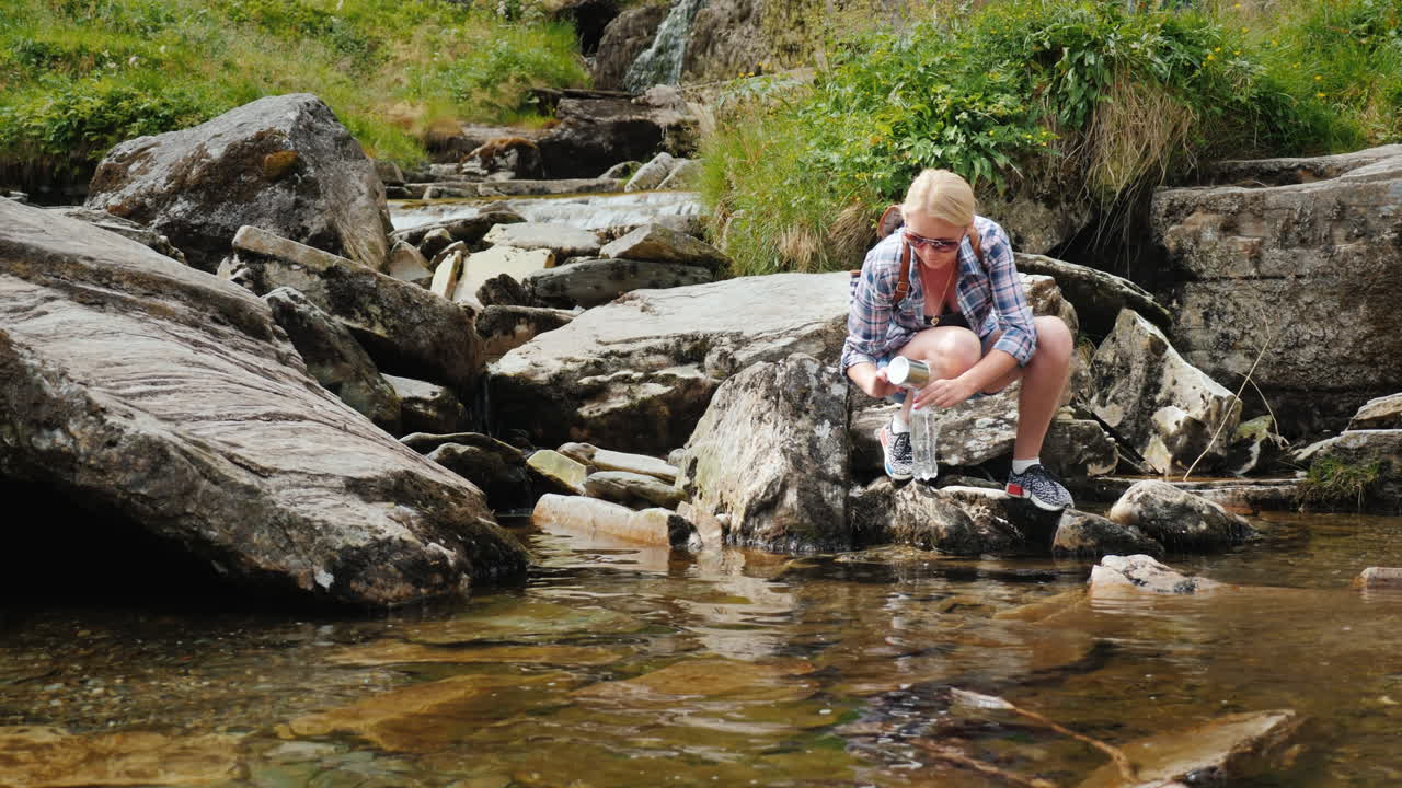 En kvinde drikker rent vand opsamlet fra en bæk ved Tvindefossen-vandfaldet i Norge 4K-video