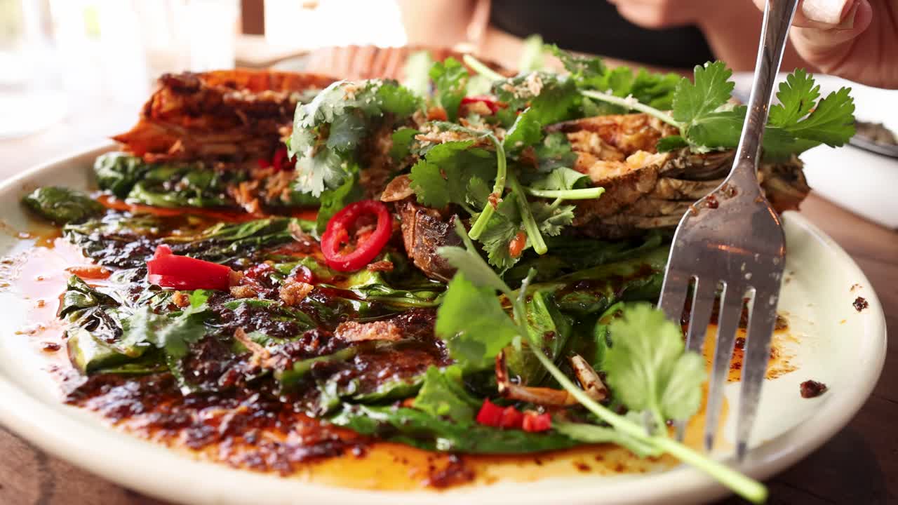 A vibrant dish of grilled mantis shrimp garnished with fresh herbs and spices, captured in a lively restaurant setting